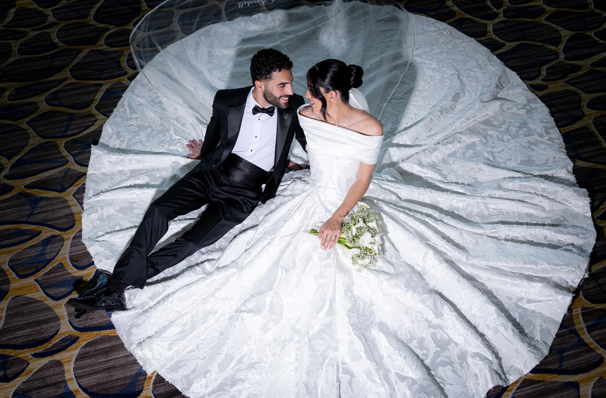 Overhead view of a bride and groom lying within her wide white gown