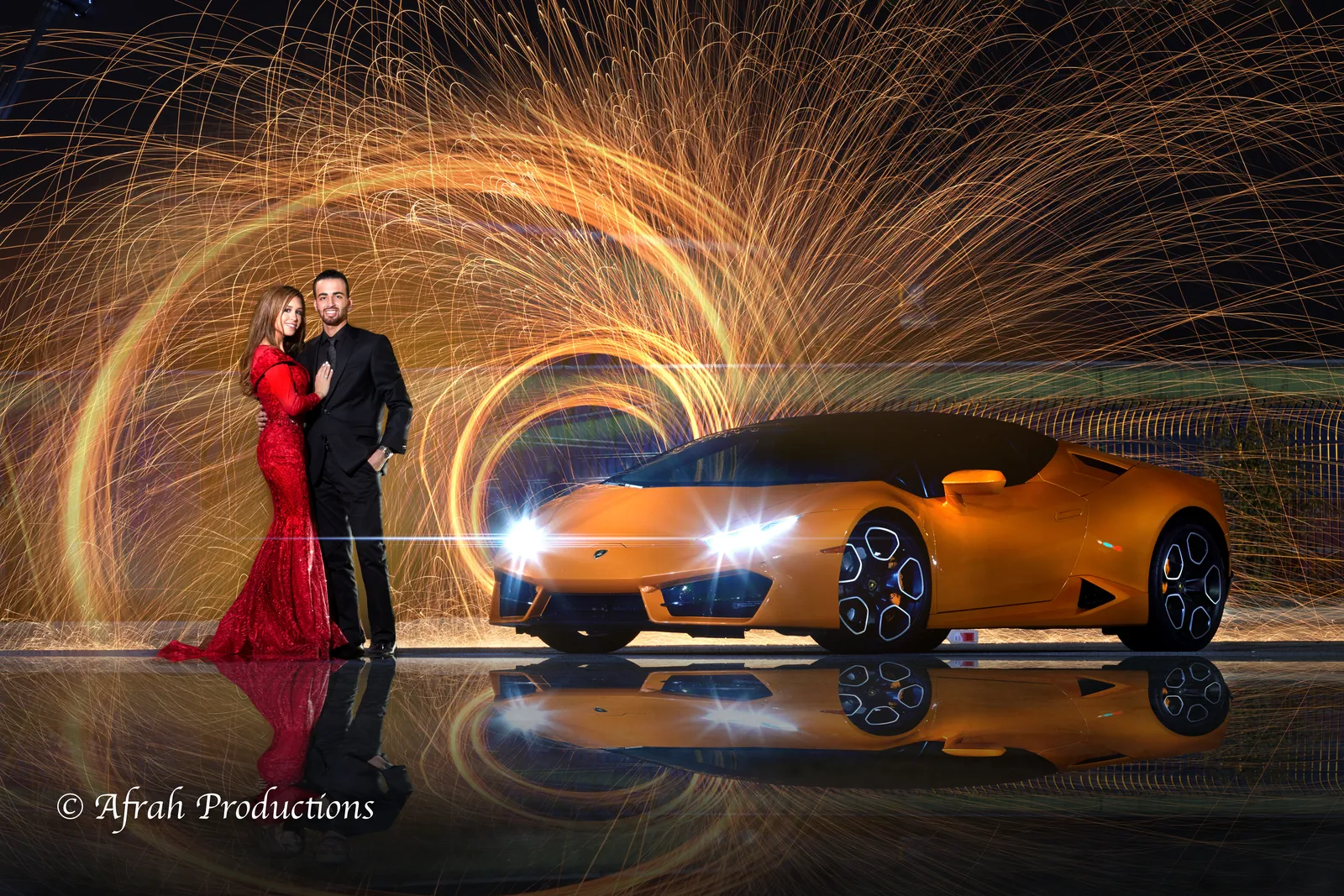 Couple beside an orange sports car with spinning sparks behind them