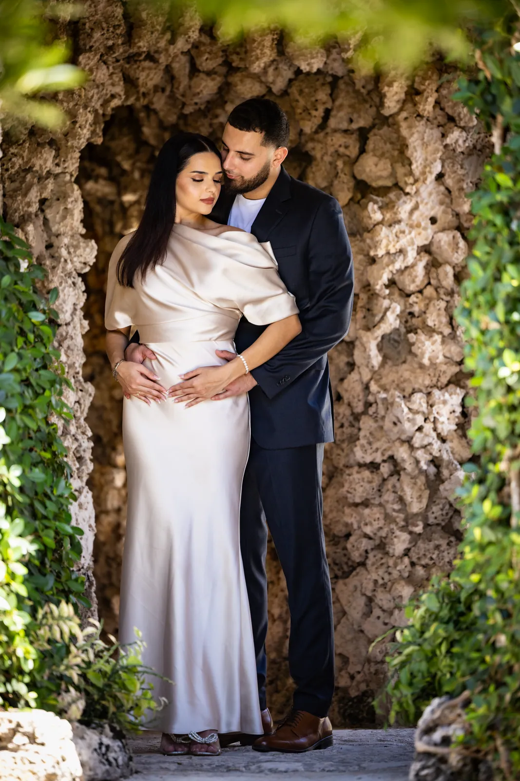 Couple embracing in a garden courtyard, bride in a long ivory gown