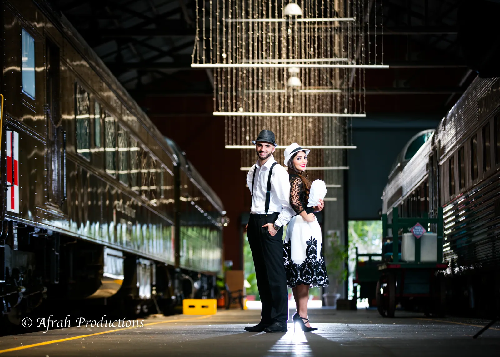 Couple beneath hanging lights between vintage train cars