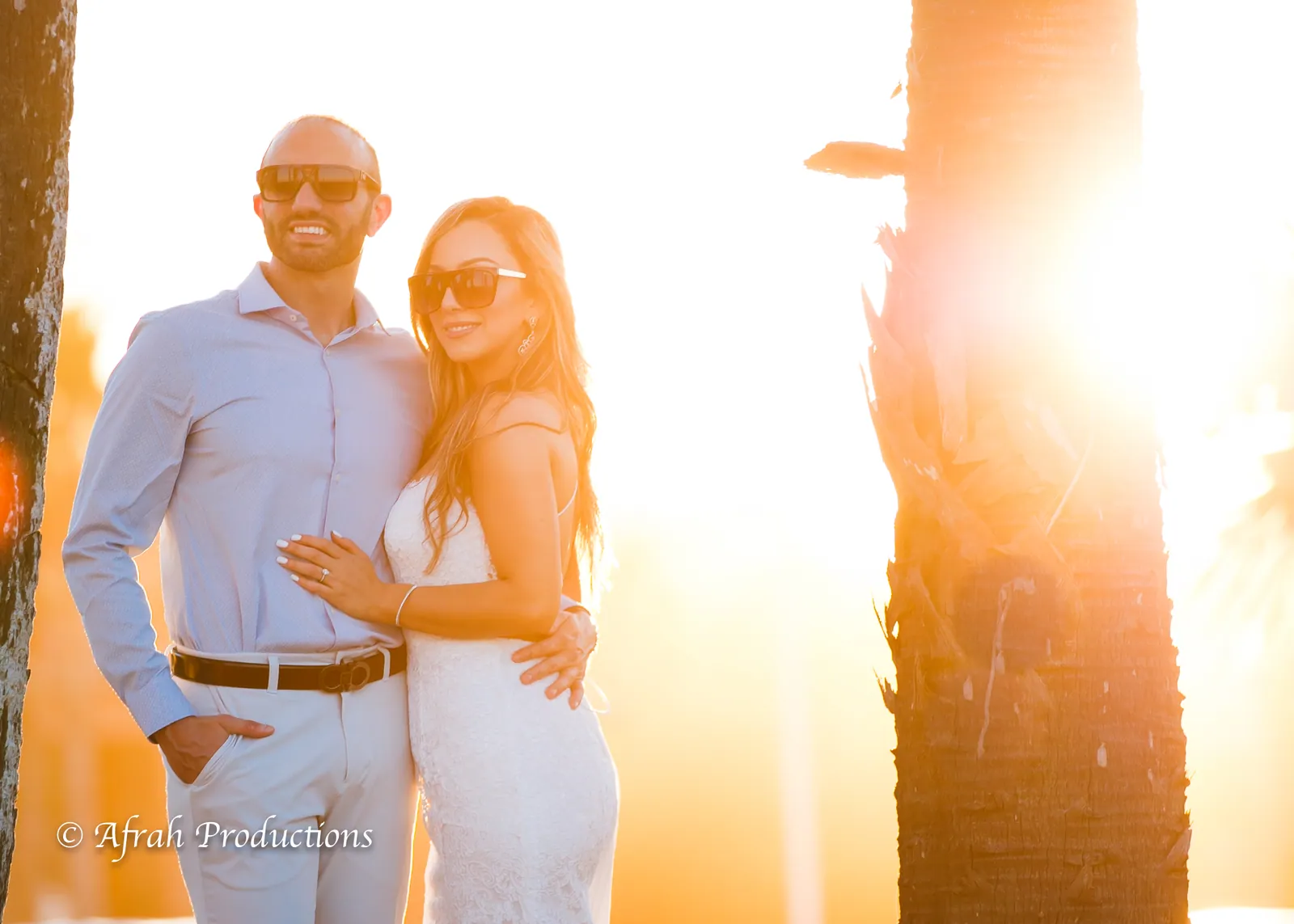 Couple against the sun between palm trunks at golden hour